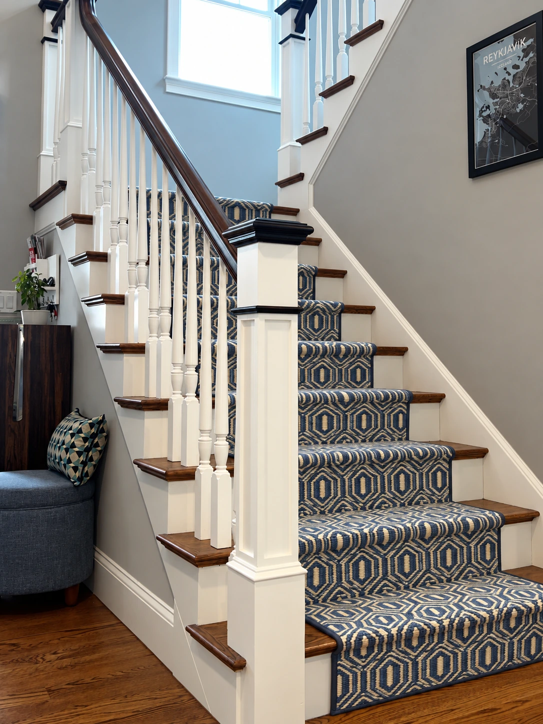 Blue and ivory geometric stair runner with coordinated edging on a white and dark wood staircase